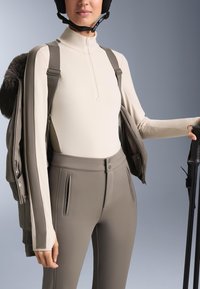 Bézs színű, cipzáros aláöltözet felső oliva zöld, testhezálló nadrággal. Texturált dzseki szőrmével díszítve. Kiegészítők között síbot és sisak található.