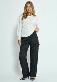 Pull en tricot blanc avec un motif texturé et des poignets côtelés, associé à un pantalon cargo noir avec des poches latérales et un tissu doux.