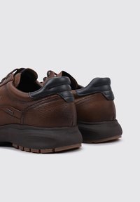 Zapatos de cuero marrón con acentos negros, que cuentan con un acabado texturizado, un cuello acolchado y una suela de goma con patrones de pisada.
