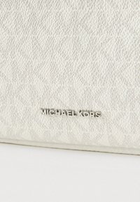 Bijela teksturirana kožna novčanik s diskretnim utisnutim uzorkom. Metalni logotip "MICHAEL KORS" na prednjoj strani. Glatka završna obrada s oblikovanom strukturom.