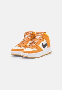 Höga sneakers i orange mocka och vit läder med svart swoosh-logotyp och orange snörning, placerade på en vit bakgrund.