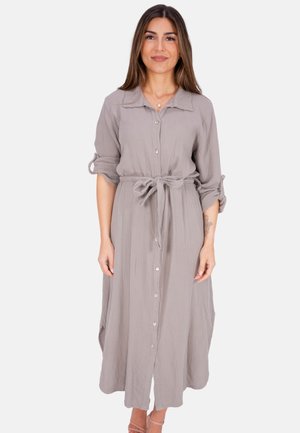 Langes, erdfarbenes, graues Hemdkleid mit kragenförmigem Ausschnitt, tailliertem Gürtel und hochgeschlagenen Ärmeln. Texturierte Stoffqualität mit sichtbaren Nähten.