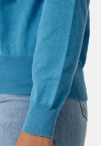 Pletený modrý svetr s žebrovanými manžetami a lemováním, který se vyznačuje jemnou strukturou a slim fit. Design obsahuje dlouhé rukávy a kulatý výstřih.