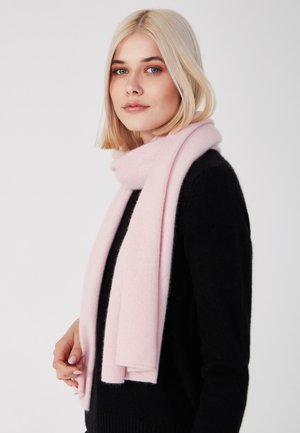 Écharpe en laine rose clair avec une texture douce, drapée autour du cou. Présentée sur un pull noir, au design épuré et simple.