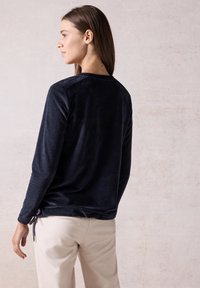 Haut à manches longues bleu marine avec une texture douce, présentant un col rond et des liens latéraux ajustables. Assorti à un pantalon beige clair.