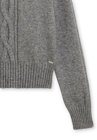 Manche de pull en tricot gris et torse inférieur avec des poignets et un ourlet côtelés, détail de tricot torsade, et petite étiquette de marque en métal rectangulaire.