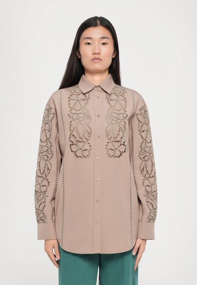 Chemise marron clair avec broderies en découpe florale sur les manches et à l'avant, manches longues, fermeture à boutons et design de col classique.