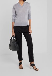Šedý svetr s výstřihem do V, černé kalhoty na míru, černá kabelka a černé sandály na vysokém podpatku se stříbrnými pásky. Hladké textury, jednoduchý design.