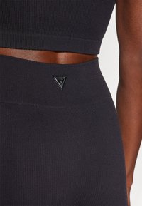 Set di top e leggings attivi neri a coste presenta un design morbido con una banda di accento bronzo e una piccola toppa triangolare con il marchio vicino alla vita.