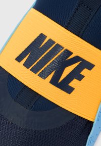 Chaussure Nike avec une tige bleu marine à finition en maille texturée, une large sangle jaune affichant un logo bleu foncé, et une semelle bleue lisse.