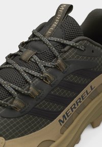 Σκούρο πράσινο παπούτσι πεζοπορίας με μπεζ σόλα, υφασμάτινο σχέδιο, χοντρά κορδόνια και το λογότυπο «MERRELL» στη πλευρά και στον θηλιά της γλώσσας.