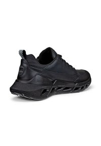 Chaussure de sport noire avec tige texturée, semelle rembourrée et design unique à découpes pour la ventilation. Accents comprenant une languette rayée au talon.