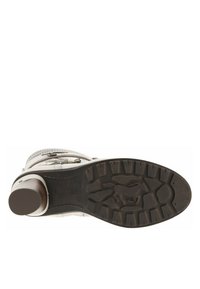 Bottine blanche à cheville avec un dessus texturé, des accents argentés et une semelle marron robuste présentant un motif strié et un détail de logo sur la semelle intérieure.