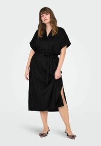 Črna obleka z pasom, kratkimi rokavi in stranskimi razporki. Tkanina ima subtilno teksturo. Usklajena z mule z leopardjim vzorcem in peto.