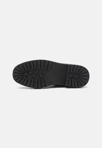 Suela de zapato de goma negra con un patrón texturizado que presenta diversas ranuras de tracción y Huecos circulares para agarre y durabilidad.