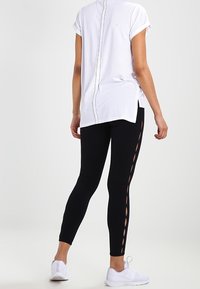 Hvid kortærmet top med en detalje i bagsømmen, parret med sorte leggings med sideudskæringer; båret med hvide sneakers.