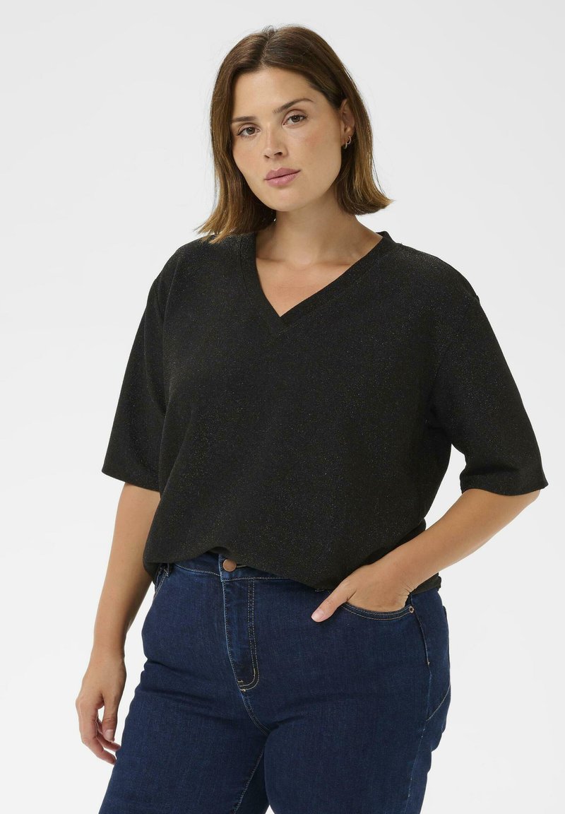Top nero a collo a V con maniche corte, realizzato in tessuto testurizzato con un leggero luccichio. Abbinato a jeans in denim blu scuro.