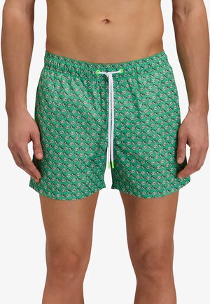 Uomo che indossa pantaloncini da bagno verdi con piccolo motivo floreale bianco e nero e coulisse bianca con punte verdi.