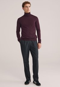 Burgundska turtleneck pulover, prilegajoča zasnova, mehak tekstur. V kombinaciji z sivimi pletnimi hlačami in črnimi supergami z belimi črtami.