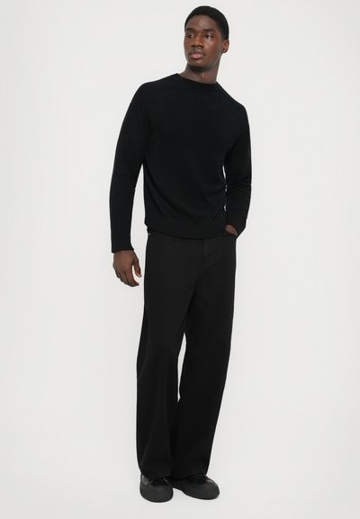 Black crewneck sweater with raglan sleeves paired with wide-leg black trousers. Both garments feature a smooth texture and minimalist design.