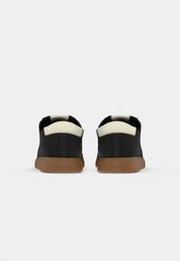 Zwarte schoenen met een textuurafwerking, witte accenten bij de hak en een gumrubberen zool. Klassiek laag ontwerp geschikt voor casual gebruik.