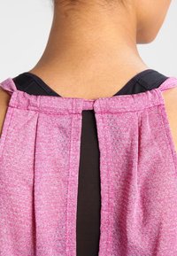 Top sin mangas de color rosa con textura y detalle plisado en la parte trasera, que presenta una capa interior negra y un corte en forma de ojo de cerradura en la parte superior de la espalda.