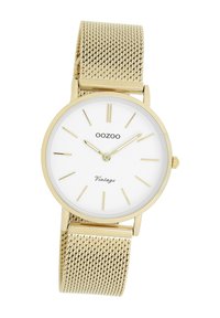 Montre avec un bracelet en mailles dorées et un cadran rond blanc. Dotée d'index et aiguilles dorés, avec "OOZOO Vintage" imprimé en dessous de la position de 12 heures.