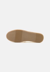 Gummisula med ett strukturerat mönster, som har en slät centrumsektion och rundade kanter, i en beige färg.