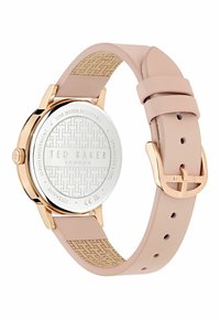 Okrúhly hodinky Ted Baker s puzdrom z ružového zlata, ružovým koženým remienkom a textúrovanou spodnou stranou. Zadná strana má vzorovanú nerezovú oceľovú konštrukciu.