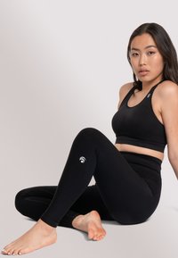 Set di abbigliamento attivo nero composto da un top corto con schiena a corsetto e leggings a vita alta. I leggings presentano un motivo testurizzato e un logo sulla caviglia.