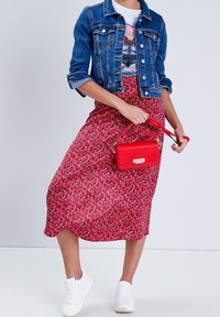 Veste en denim au design ajusté, associée à une jupe midi rouge à fleurs, des baskets blanches et un petit sac rouge. Textures lisses et couleurs vives.
