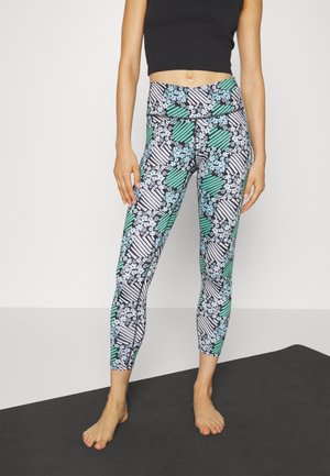 Leggings multicolores présentant un motif floral et rayé en noir, blanc et vert. Fabriqués à partir d'un matériau léger et flexible.