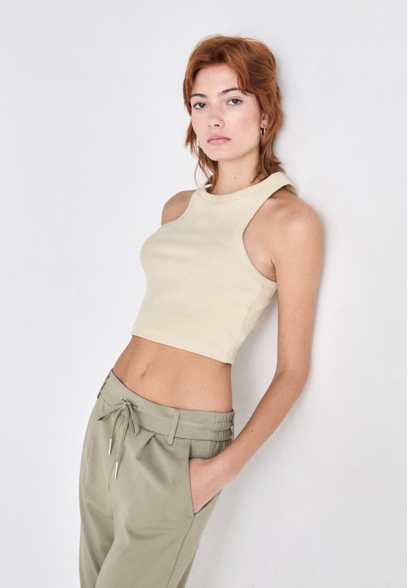 Beige geripptes Crop-Top mit rundem Ausschnitt, kombiniert mit hellgrünen, Bund mit Kordelzug Hosen mit seitlichen Taschen. Glatte Textur.