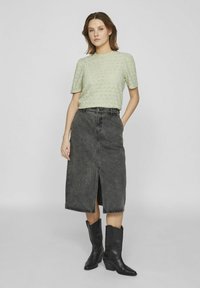 Heled roheline lühikeste varrukatega kudum, millel on teemantmuster; must denimsinine midi seelik, millel on esisisselõige; mustad terava ninaga cowboy-saapad.