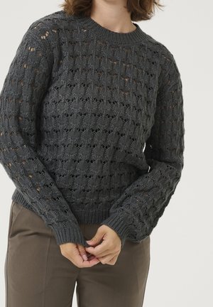 Pull en maille grise avec un motif en dentelle, col rond et poignets et ourlet côtelés. La texture semble douce, avec une légère transparence dans le tissu.