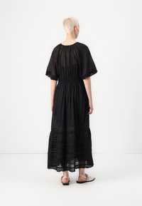 Robe maxi noire avec de courtes manches flottantes, taille smockée et jupe superposée. Fabriquée en tissu léger avec une bordure en dentelle à l'ourlet.