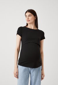 Črn kratkolasni materinski zgornji del s ukrivljenim robom, mehko teksturo in prileganjem kroju, v kombinaciji s svetlo modrimi kavbojkami.