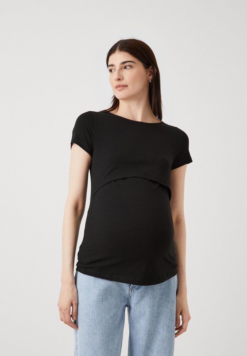 Črn kratkolasni materinski zgornji del s ukrivljenim robom, mehko teksturo in prileganjem kroju, v kombinaciji s svetlo modrimi kavbojkami.