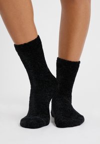 Czarne, puszyste skarpetki o miękkiej strukturze, sięgające do połowy łydki, z prążkowanym wzorem. Gładkie szwy palców i gruby materiał zapewniający ciepło.