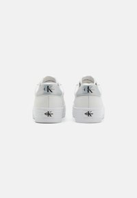 White sneakers with a smooth leather upper, thick rubber sole, embossed logo on heel, silver accents, and textured detailing on the sole.