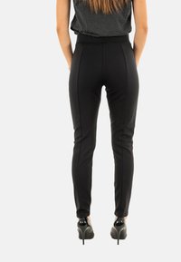 Pantaloni neri attillati con una texture liscia, caratterizzati da strisce laterali e una vita alta. Abbinati a tacchi neri lucidi.
