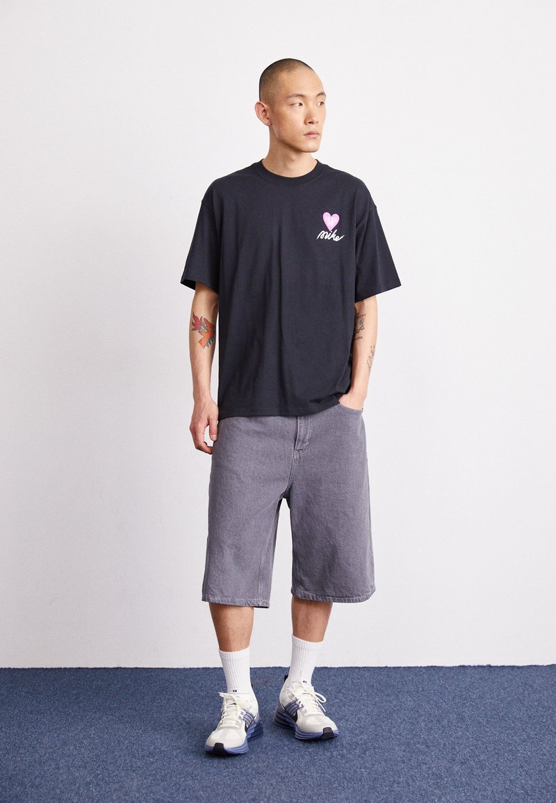 Camiseta de algodón negra con gráfico "love Nike" en rosa, combinada con shorts de mezclilla gris y calcetines deportivos blancos, que lucen sneakers grises.