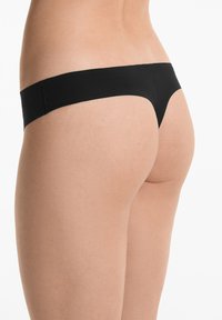 Zwarte thong ondergoed gemaakt van soepel materiaal met minimale bedekking, met een naadloos ontwerp en een zachte elastische tailleband.