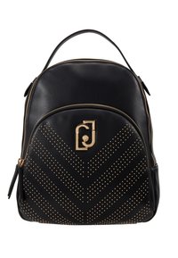 Mochila de cuero negro con herrajes dorados, que presenta un patrón de chevrón de tachuelas y un bolsillo con cremallera frontal. Asa superior para transportar.