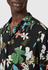 Czarna koszula z krótkim rękawem z kwiatowym nadrukiem w zielone, niebieskie, czerwone i białe kwiaty. Zapinana na guziki z wyszywanym logo.