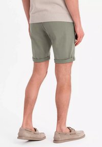 Shorts vert olive avec des ourlets roulés, fabriqués en tissu de coton doux. Associés à des chaussures en daim beige. Accent sur la silhouette et la texture.