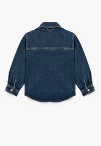 Denimskjorte i mørkeblå, med spidse kraver, lange ærmer med knapmanchetter og en buet kant. Bagudvisning viser en syet søm tværs over skuldrene.
