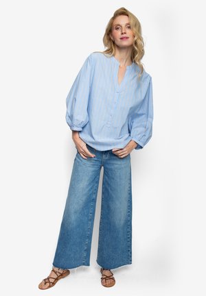 Hellblaue Bluse mit Streifen, Kragen, Knopfleiste und Puffärmeln, kombiniert mit weit geschnittenen Jeans und flachen Sandalen.