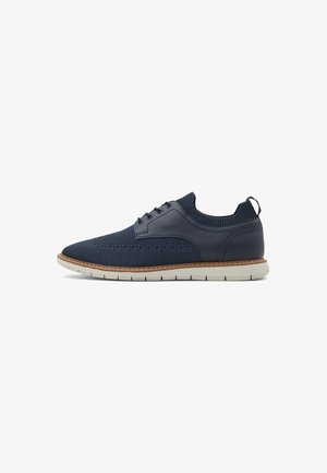 Navy blue sneaker featuring woven mesh and smooth leather with a white sole. Accents include a stitched edge and a small heel tab.