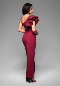Robe de soirée bordeaux à une épaule, avec un détail volanté. Le tissu est lisse avec une silhouette cintrée et une fente latérale.